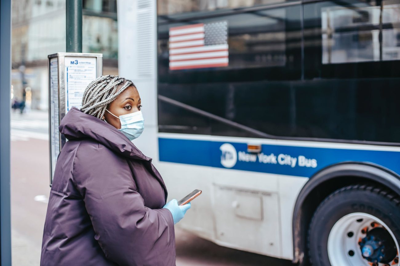Une femme devant un bus avec son téléphone à la main