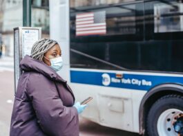 Une femme devant un bus avec son téléphone à la main